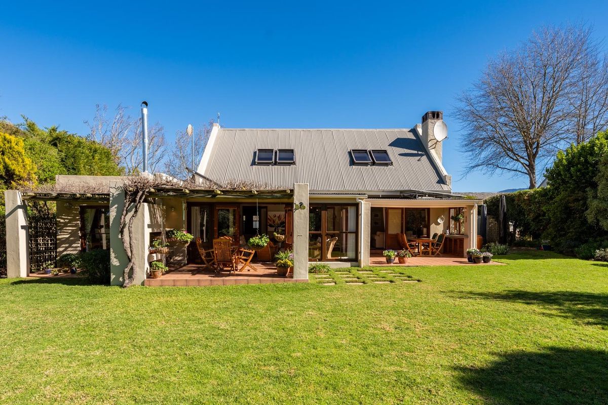 Rear view of the house featuring a spacious covered patio, large sliding glass doors, and a well-maintained garden with a corrugated metal roof.