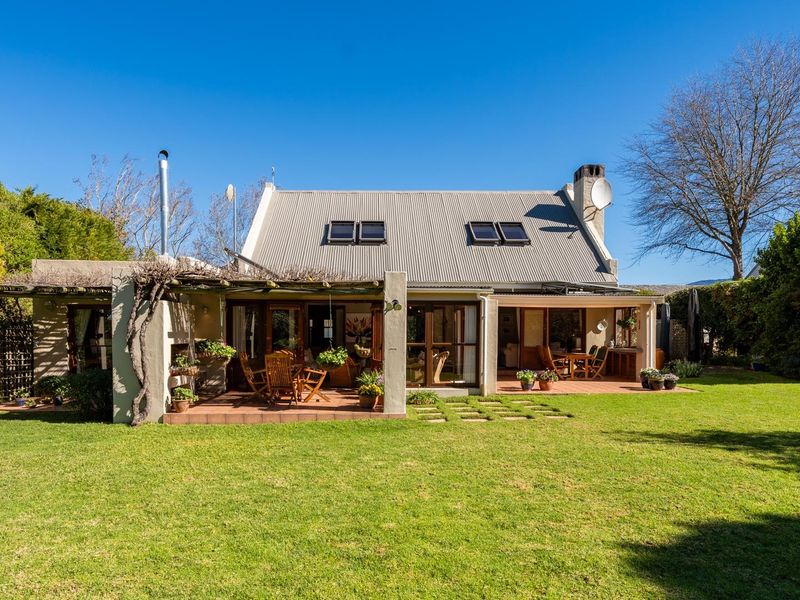 Rear view of the house featuring a spacious covered patio, large sliding glass doors, and a well-maintained garden with a corrugated metal roof.