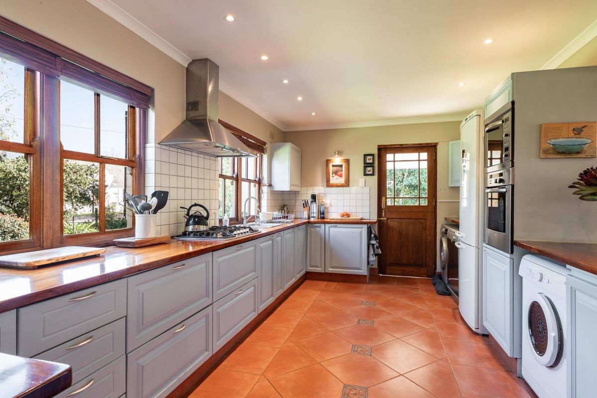 A well-maintained kitchen featuring wooden countertops, a gas hob, stainless steel extractor, built-in oven, and classic terracotta-style tiled flooring with timber accents.