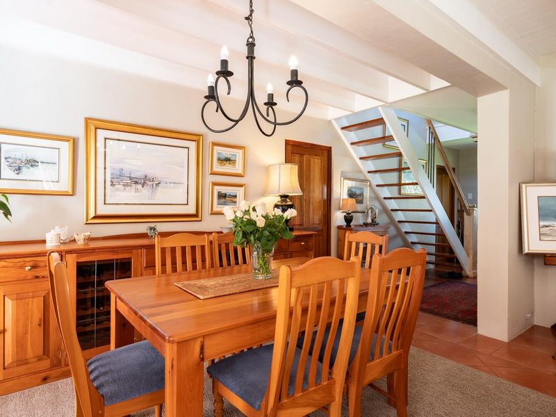 A warm dining area featuring exposed timber ceiling beams, terracotta flooring, and a classic timber staircase leading to the upper level.