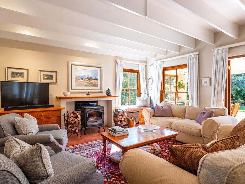 Spacious living room featuring exposed timber ceiling beams, a cast iron wood-burning stove, terracotta flooring, and direct access to the garden through timber doors.