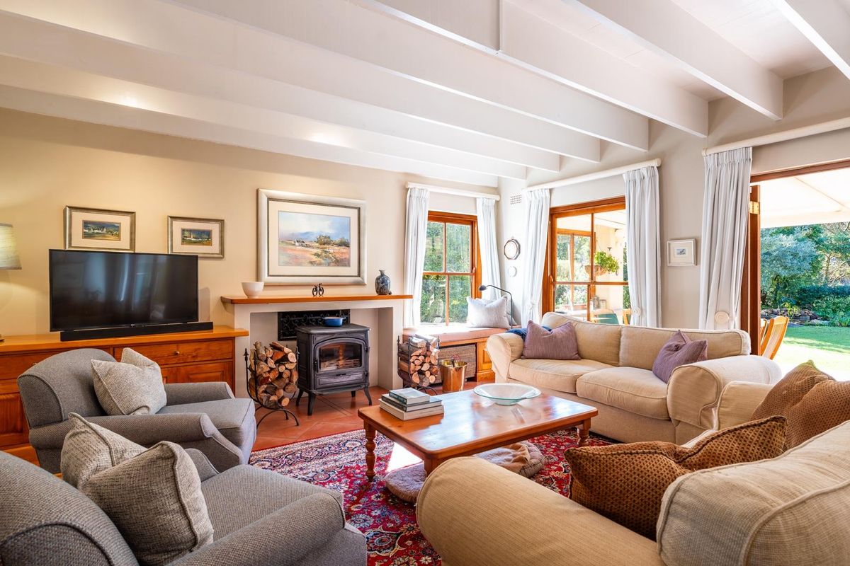 Spacious living room featuring exposed timber ceiling beams, a cast iron wood-burning stove, terracotta flooring, and direct access to the garden through timber doors.