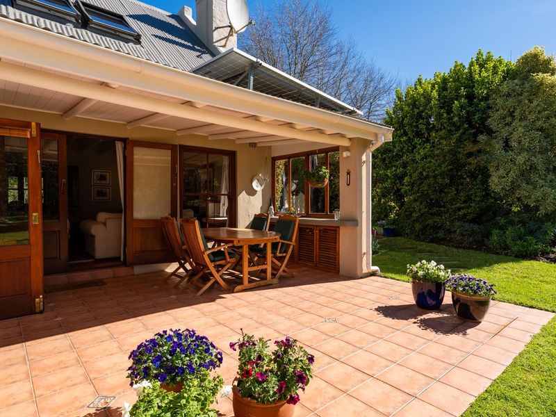 A spacious covered patio featuring tiled flooring, timber-framed doors, and built-in cabinetry, overlooking a well-maintained garden area.