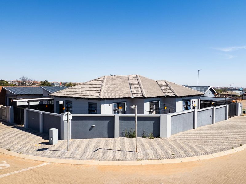 An elevated view of a modern residential property featuring a tiled roof, secure perimeter wall with electric fencing, and a paved driveway.