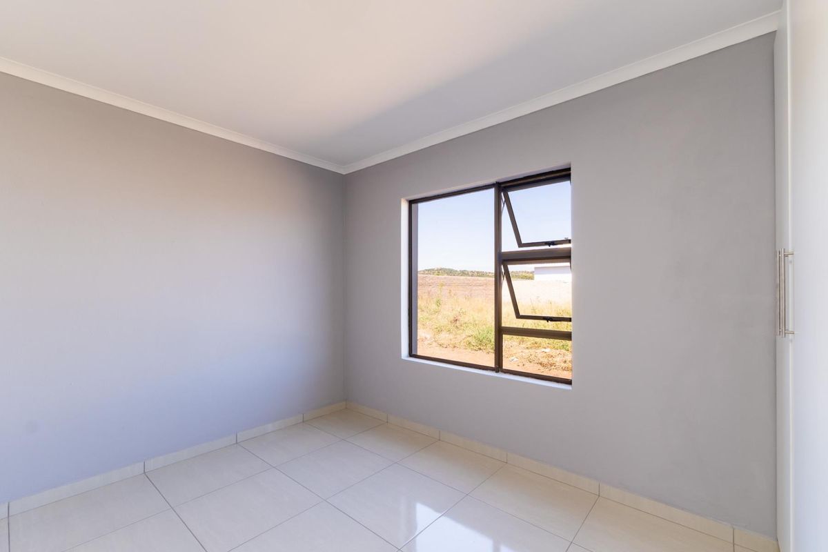 A bright, empty bedroom featuring neutral grey walls, tiled flooring, and a built-in cupboard with an aluminium-framed window.