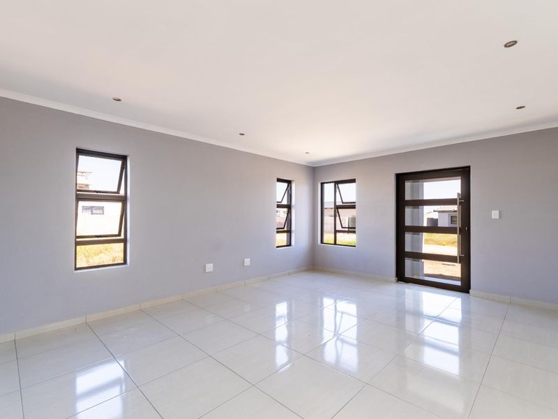 A bright, vacant living area featuring neutral grey walls, polished porcelain floor tiles, recessed lighting, and modern aluminium-framed windows and door.