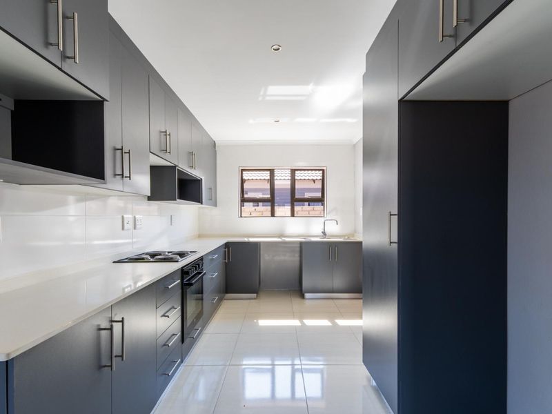 Modern galley-style kitchen featuring sleek dark cabinetry, stone countertops, integrated oven and hob, and polished tiled flooring in a bright, clean space.