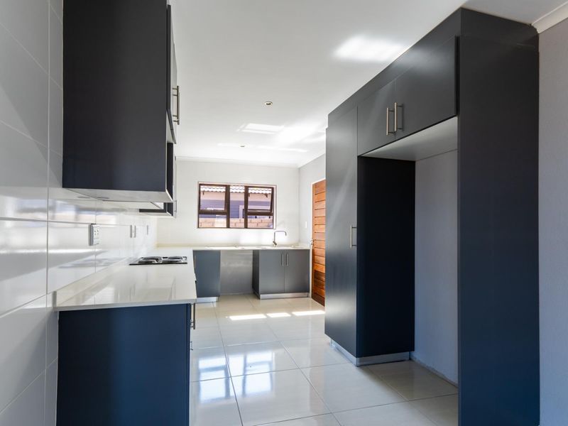 Modern kitchen featuring dark cabinetry, white quartz countertops, tiled flooring, and a built-in hob, offering a clean and functional workspace.
