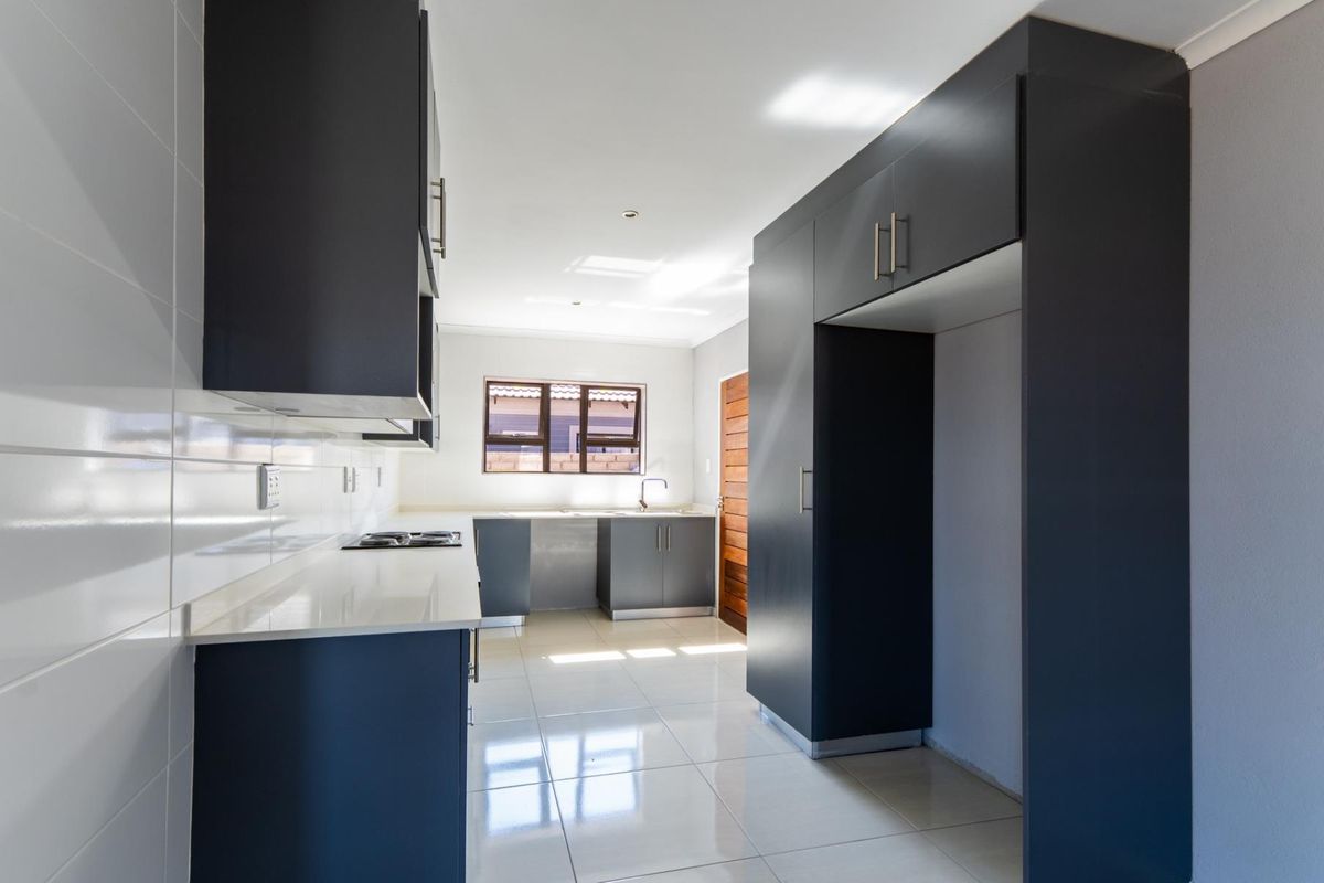 Modern kitchen featuring dark cabinetry, white quartz countertops, tiled flooring, and a built-in hob, offering a clean and functional workspace.