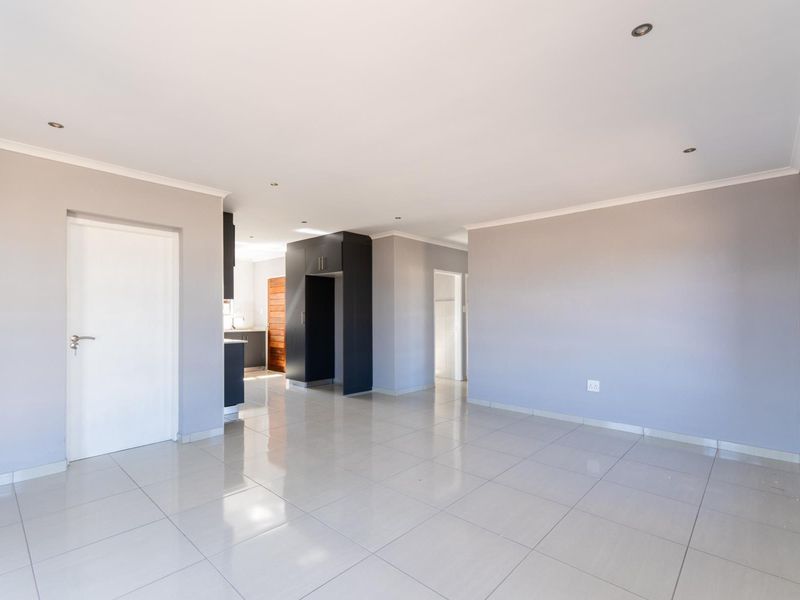 Spacious open-plan living area featuring neutral grey walls, polished tiled flooring, and recessed downlights, seamlessly connecting to a modern kitchen space.