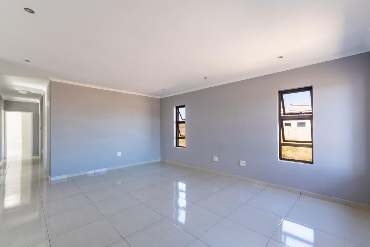 A bright, empty living room featuring neutral grey walls, polished tiled flooring, and modern aluminium windows with recessed ceiling lighting.