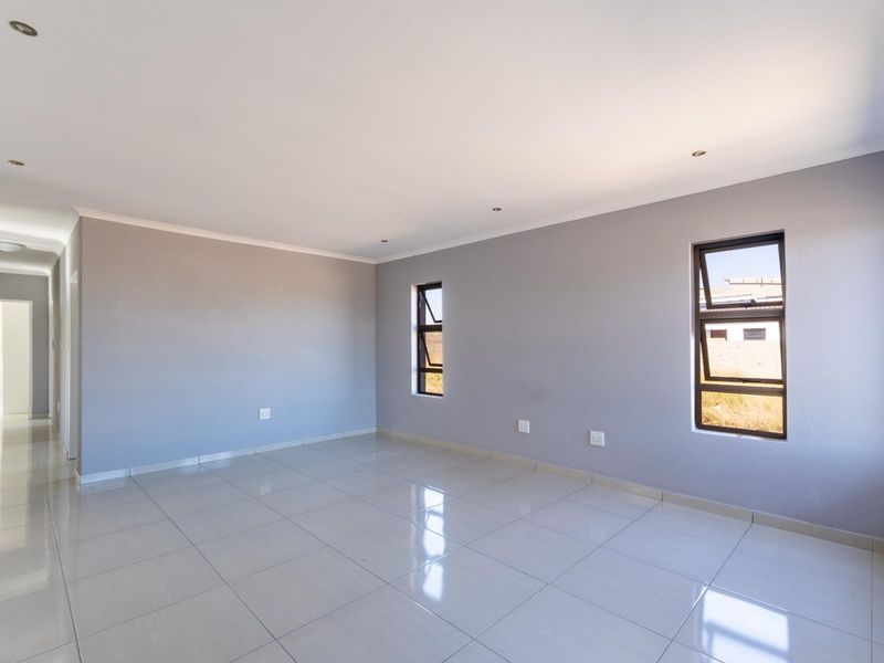 A bright, empty living room featuring neutral grey walls, polished tiled flooring, and modern aluminium windows with recessed ceiling lighting.