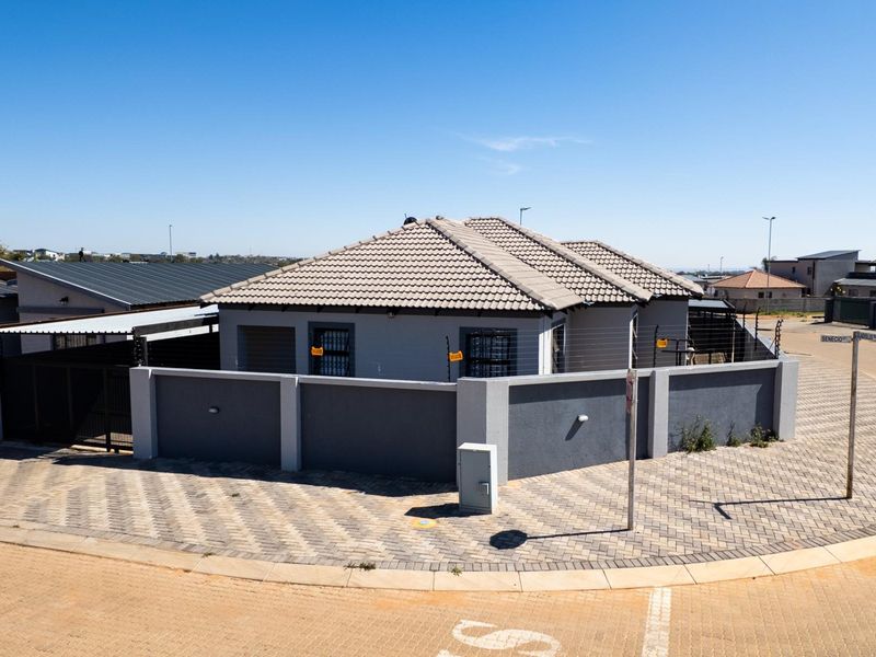 A corner-lot residential property featuring a tiled roof, secure perimeter wall with electric fencing, and paved driveway access.