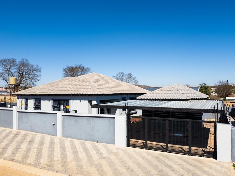 Front exterior view of a well-maintained house featuring a paved driveway, secure perimeter wall with electric fencing, and a covered carport.