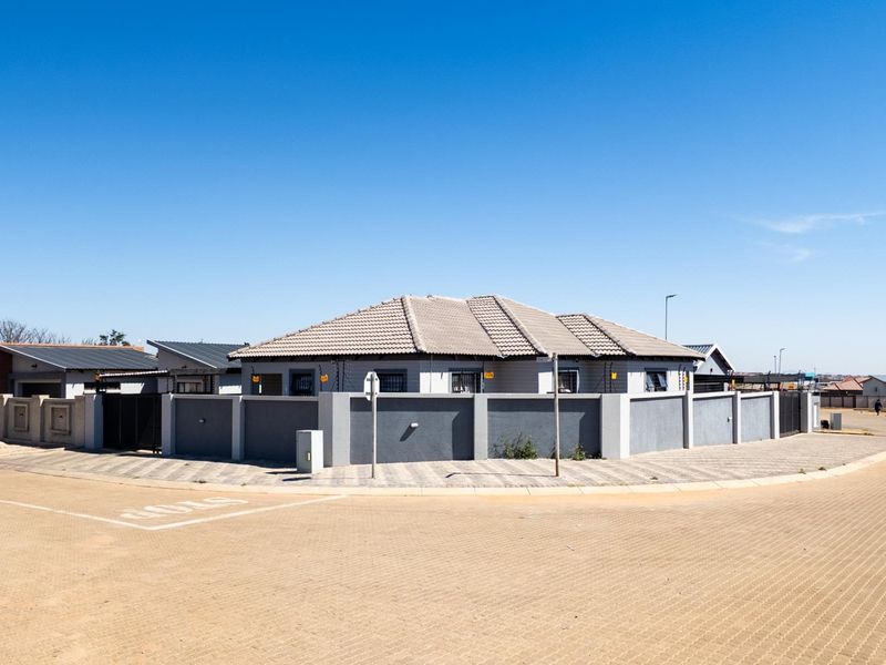 A corner-lot residential property featuring a secure perimeter wall, tiled roof, and paved driveway in a well-maintained suburban setting.