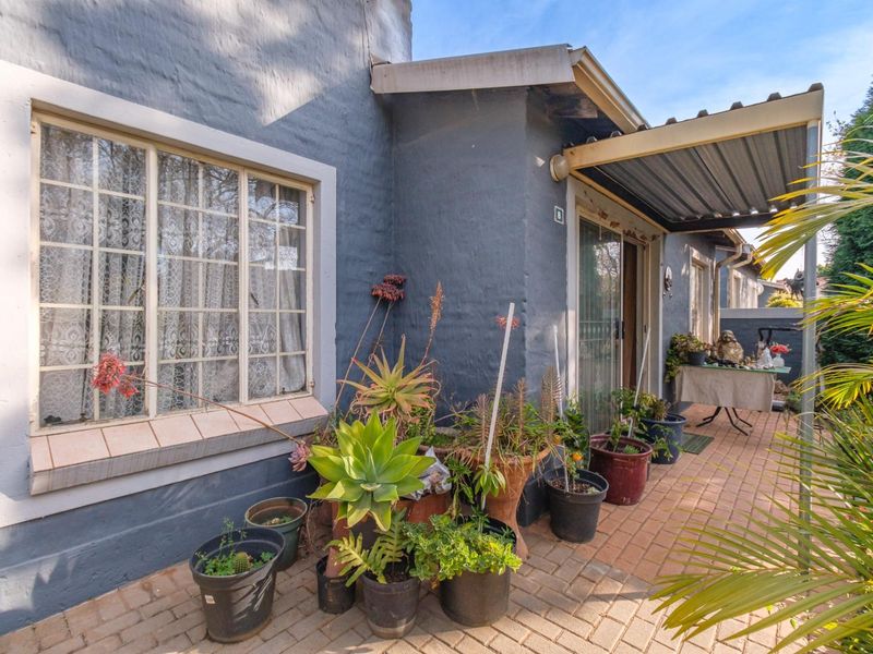 A paved outdoor patio area featuring a covered roof section, sliding glass door access, and classic grid-pattern windows on the exterior wall.