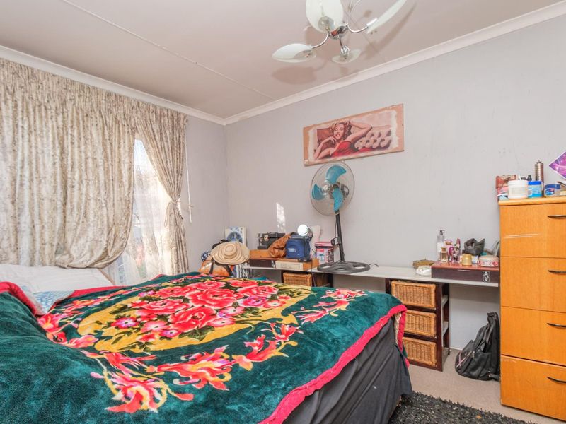 A bedroom featuring a ceiling fan and window curtains, requiring cosmetic updates to the wall finishes to improve the overall aesthetic.