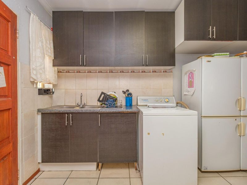 Compact laundry area featuring dark built-in cabinetry, laminate countertops, a stainless steel sink, and tiled backsplash.