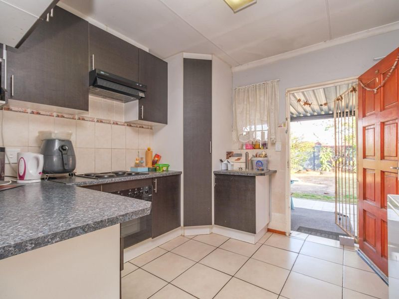 Functional kitchen featuring dark cabinetry, laminate countertops, built-in oven and hob, tiled flooring, and direct access to the rear outdoor area.