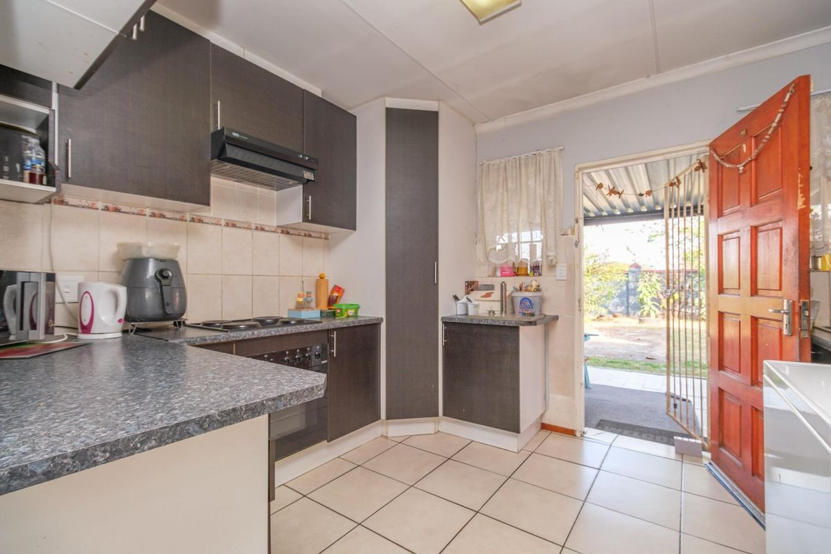 Functional kitchen featuring dark cabinetry, laminate countertops, built-in oven and hob, tiled flooring, and direct access to the rear outdoor area.
