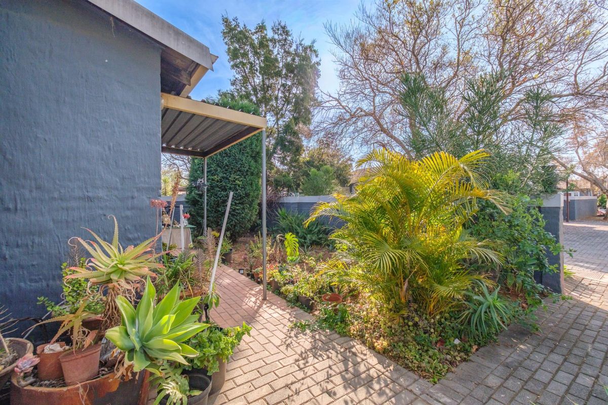 A private rear garden area featuring a paved walkway, established landscaping, and a small covered patio structure attached to the townhouse.