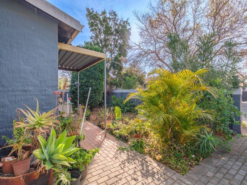 A private rear garden area featuring a paved walkway, established landscaping, and a small covered patio structure attached to the townhouse.