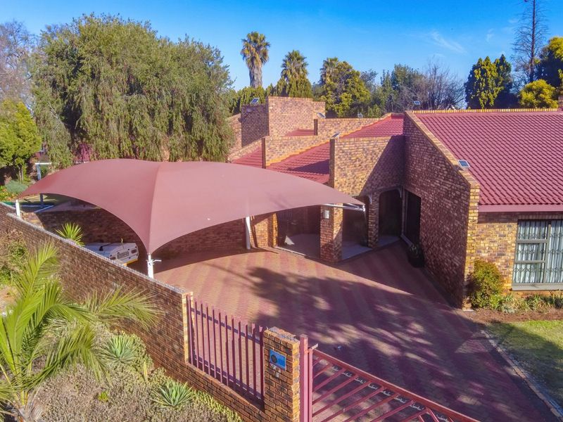 Aerial view of a face brick house featuring a paved driveway, shade sail carport, and secure perimeter fencing.