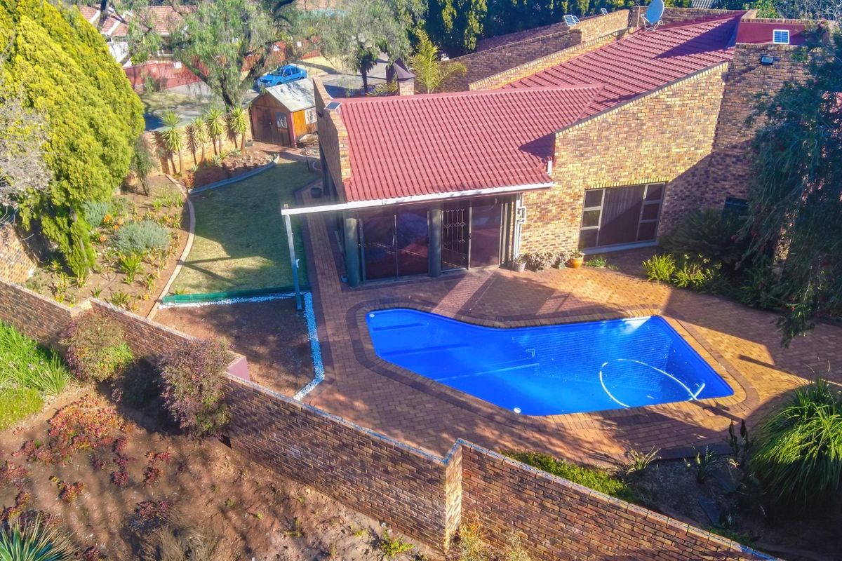 Aerial view of the property featuring a swimming pool, paved patio area, and established garden with brick boundary walls.