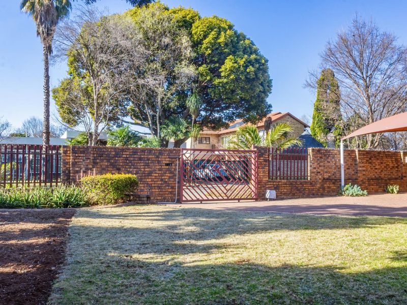 Front view of the property featuring a brick boundary wall, metal driveway gate, paved driveway, and a shade sail over the parking area.
