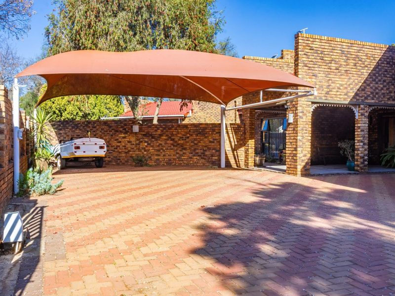Rear exterior area featuring brick paving, a shade sail carport, and a covered patio attached to the main brick building structure.