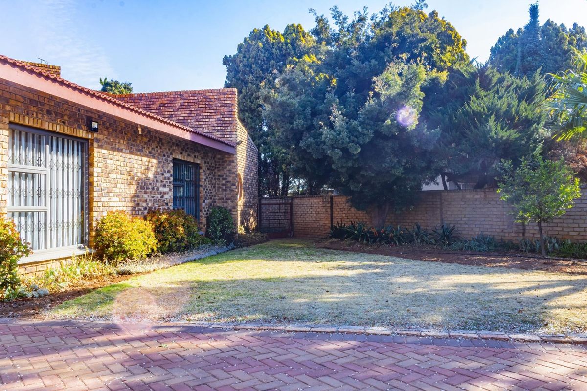 A private rear garden featuring a paved area, established trees, and a face brick exterior wall with security-fitted windows.