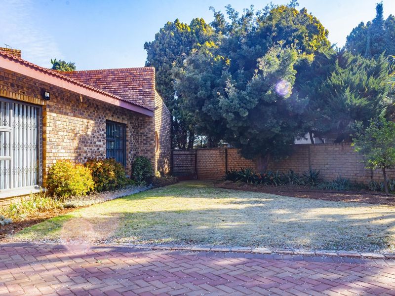 A private rear garden featuring a paved area, established trees, and a face brick exterior wall with security-fitted windows.