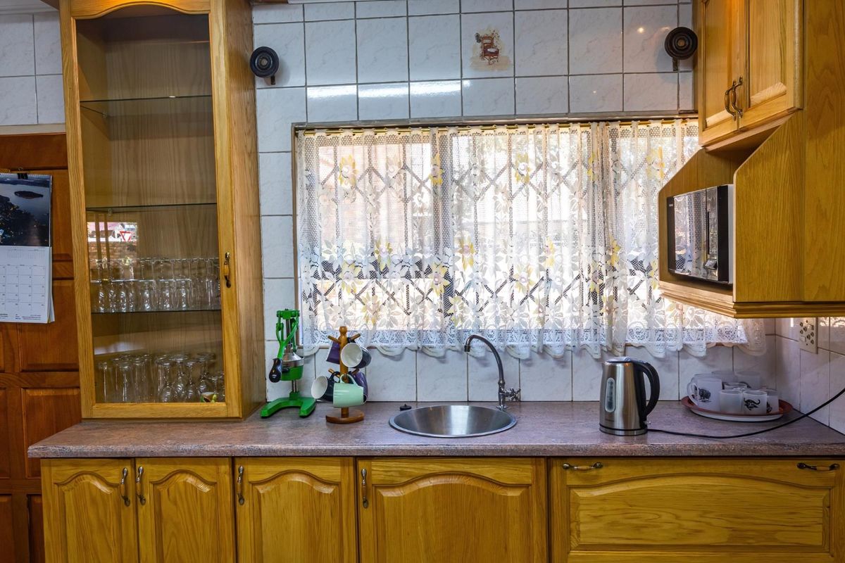 A traditional kitchen featuring timber cabinetry, laminate countertops, a stainless steel sink, and tiled splashbacks, offering a functional and classic workspace.