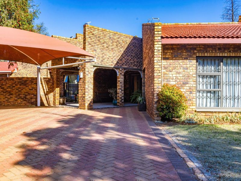 Front exterior view of a face brick house featuring a paved driveway, covered entrance, and a shade sail structure.