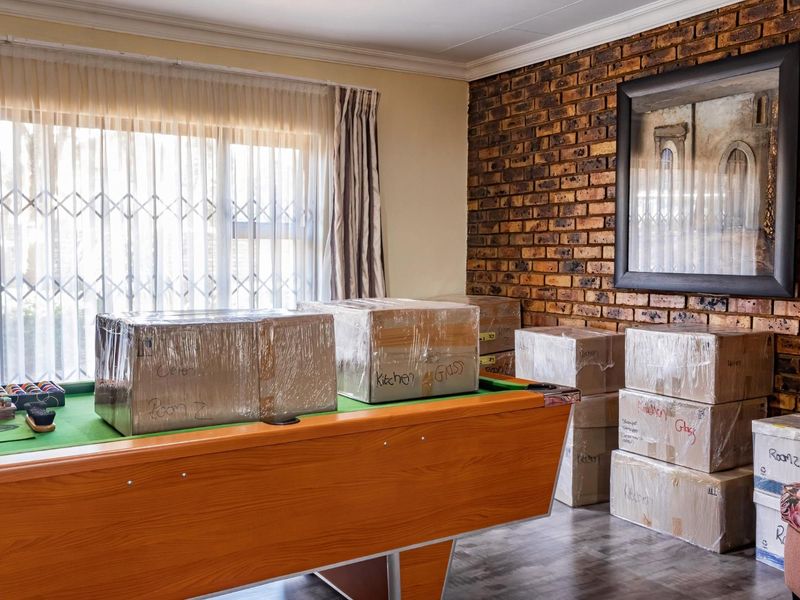 Living area featuring an exposed brick feature wall, laminate flooring, and a security gate over the window.