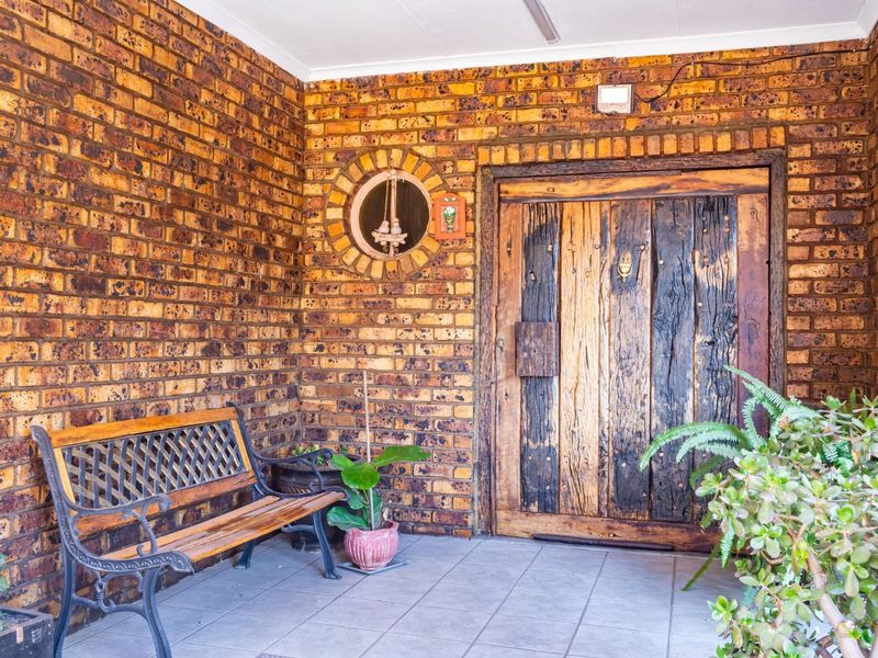 Covered entrance porch featuring rustic exposed brick walls, tiled flooring, and a distinctive solid timber front door with a circular accent window.