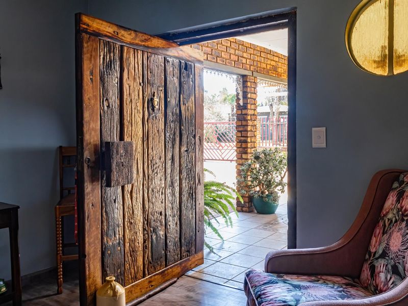 An inviting entryway featuring a unique, rustic timber door opening onto a covered brick-pillared patio area.