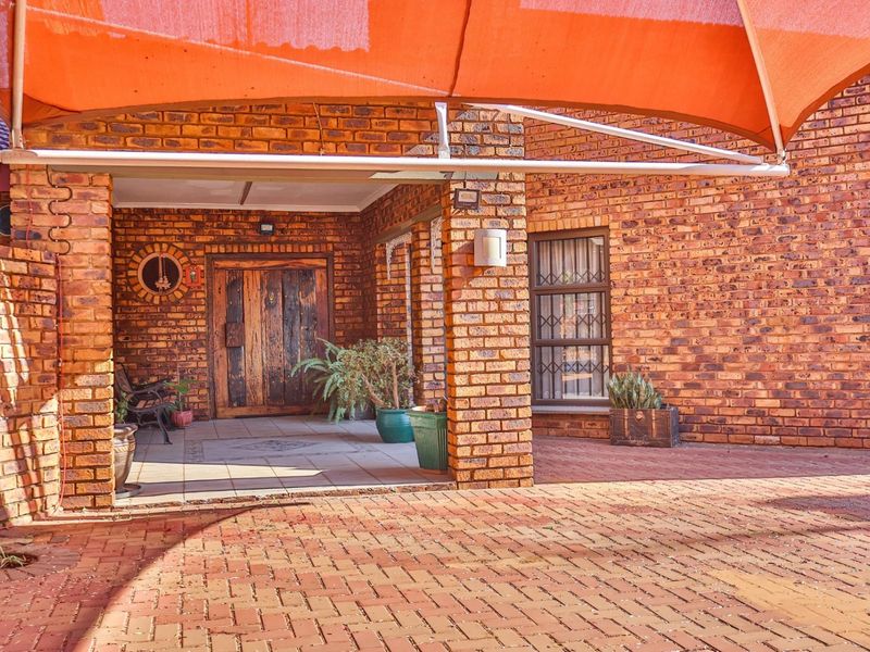 A covered patio area featuring face brick construction, paved flooring, and a large orange shade sail providing outdoor shelter.
