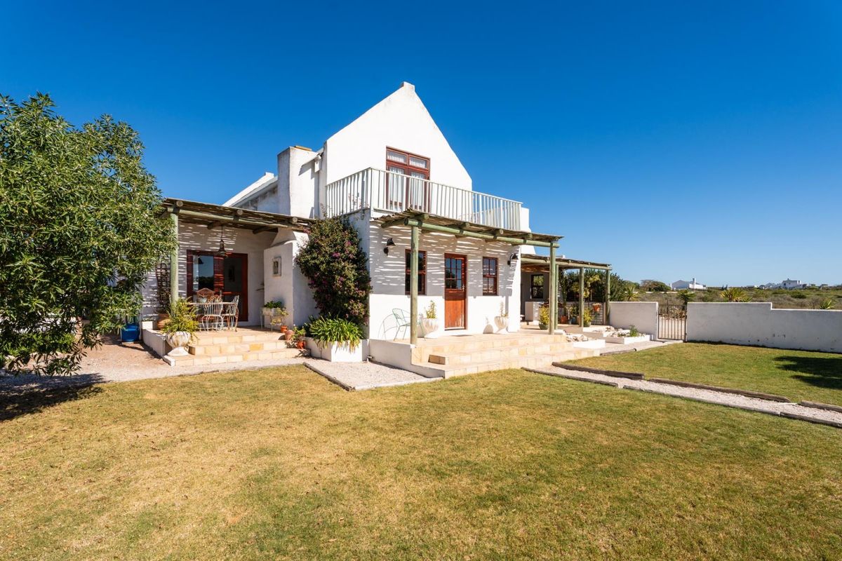 Rear view of a white-walled cottage featuring a timber pergola, stone patio, and an upper-level balcony overlooking the garden.