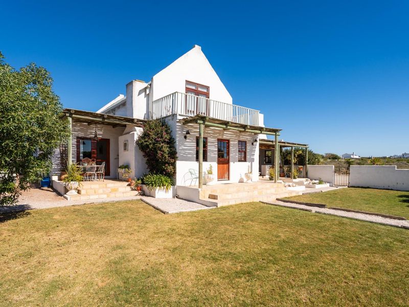 Rear view of a white-walled cottage featuring a timber pergola, stone patio, and an upper-level balcony overlooking the garden.