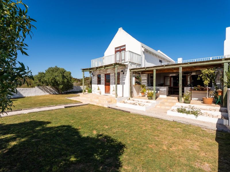 Rear view of a white-walled property featuring a covered patio, timber pergola, upper-level balcony, and a well-maintained garden area.