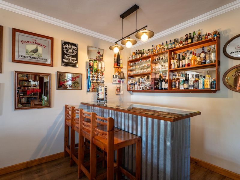 A dedicated home bar area featuring a corrugated metal counter, custom wall-mounted shelving for glassware and bottles, and stylish pendant lighting.