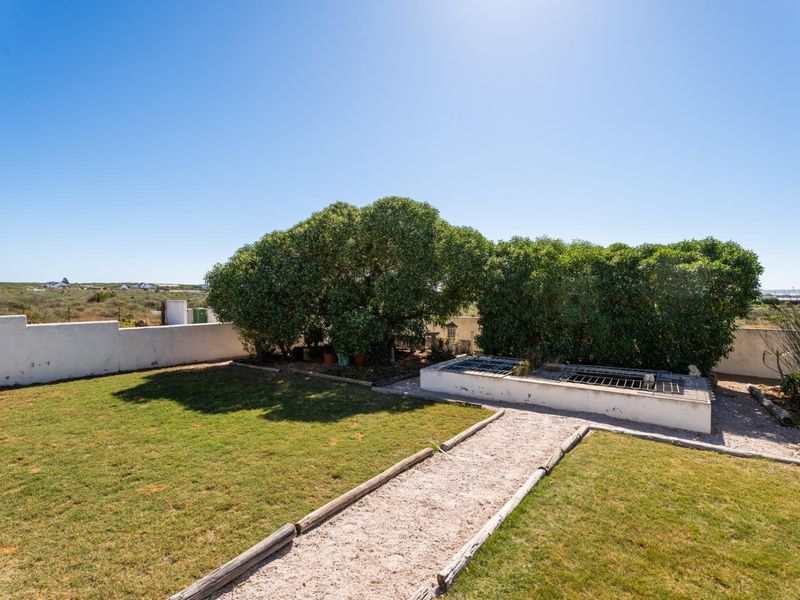 A well-maintained garden area featuring a gravel pathway, established greenery, and a raised concrete planter structure against a boundary wall.