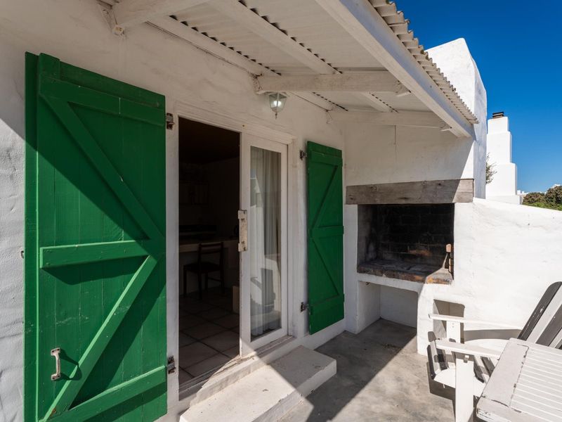 Covered patio area featuring a built-in braai, concrete flooring, and distinctive green timber shutters providing access to the interior.