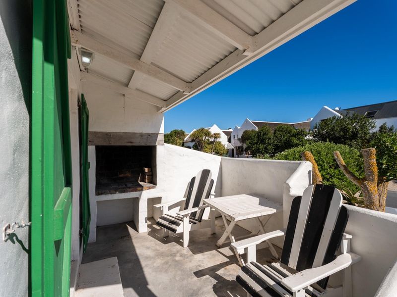 A covered outdoor patio featuring a built-in braai area, concrete flooring, and a white masonry wall, perfect for outdoor entertaining.