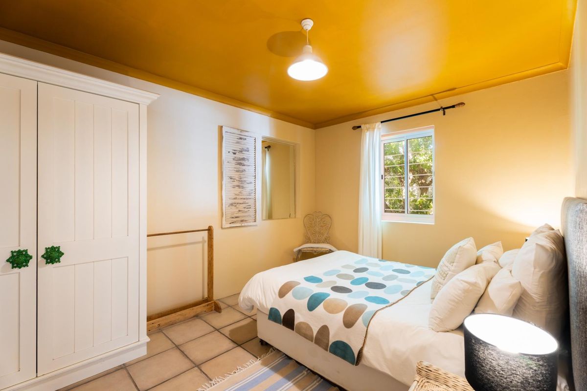 A bedroom featuring tiled flooring, a built-in wardrobe, and a window with security bars, finished with a bold yellow ceiling.