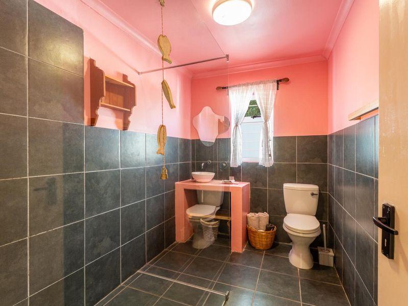 A bathroom featuring dark floor-to-ceiling wall tiles, a built-in vanity with a vessel sink, and a glass shower screen.
