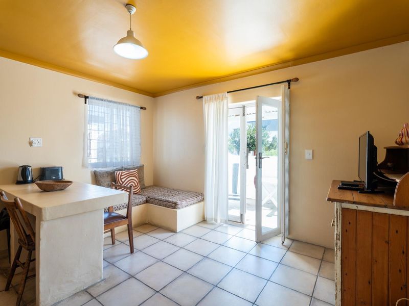 A functional living area featuring tiled flooring, built-in bench seating, a breakfast bar, and direct access to an outdoor patio through a glass door.