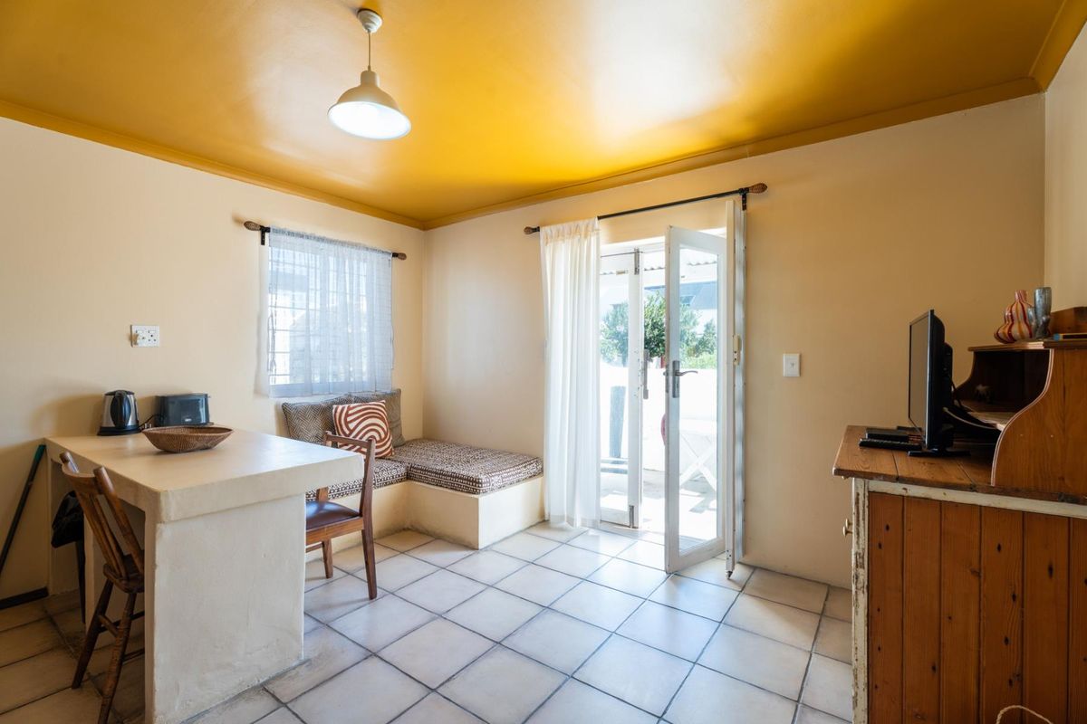 A functional living area featuring tiled flooring, built-in bench seating, a breakfast bar, and direct access to an outdoor patio through a glass door.