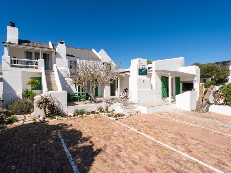 Front elevation of a white stucco house featuring a brick paved driveway, external staircase, balcony, and an outdoor fireplace area.